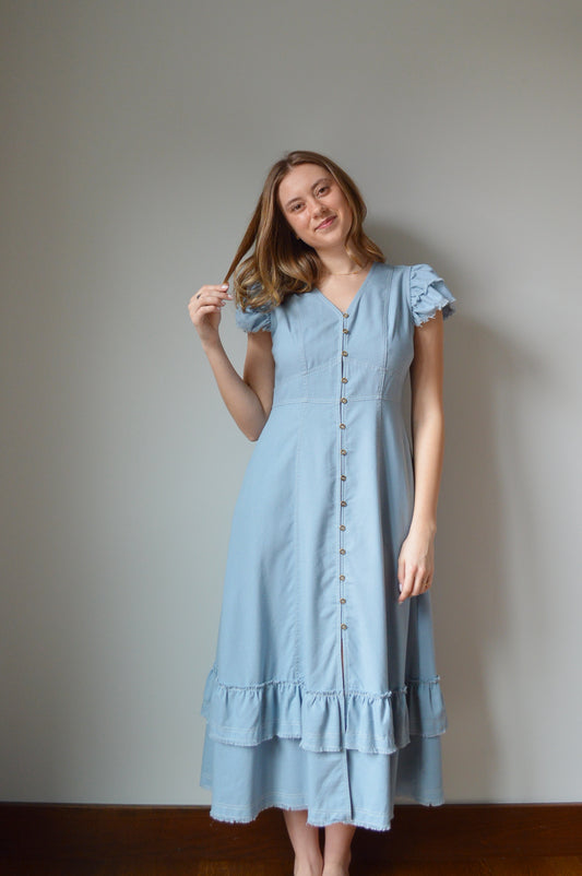 Woman wearing a light blue mid length dress standing against a grey background 