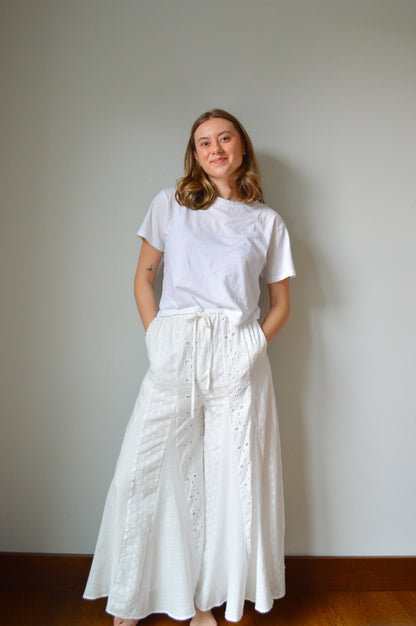 Woman wearing white eyelet wide leg pants standing against a plain background
