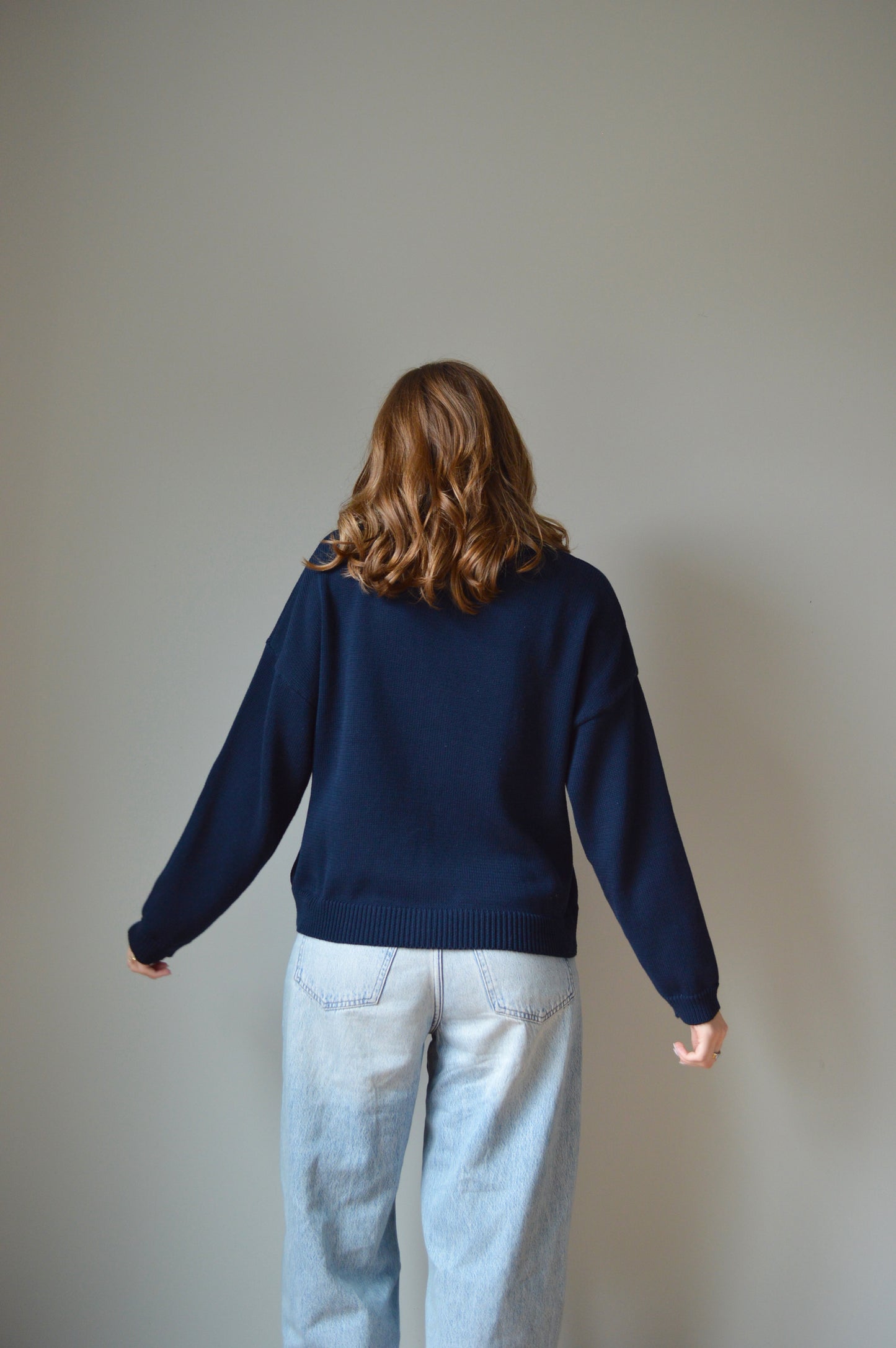 Person wearing a navy sweater and light blue pants on a plain background