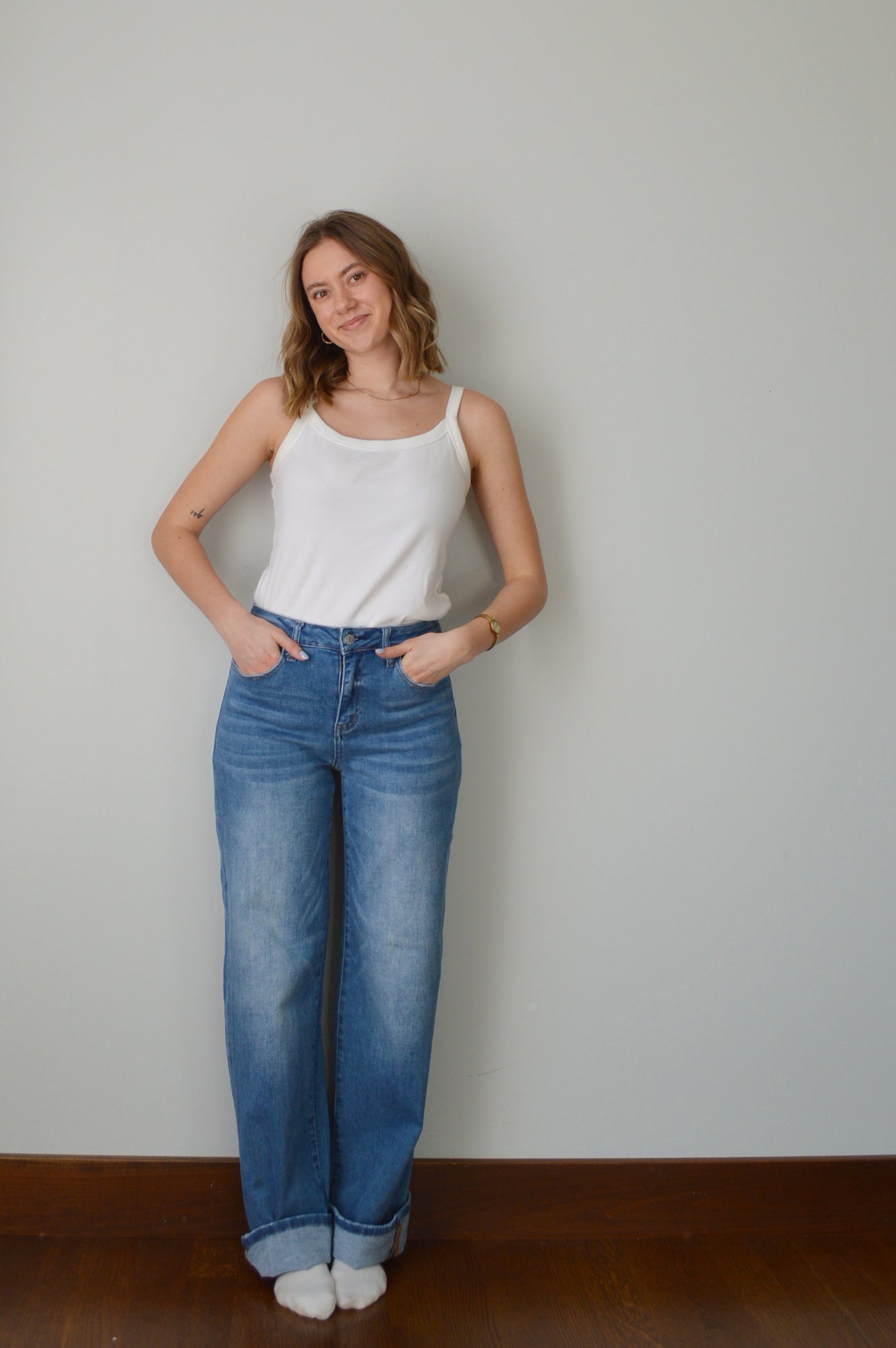 Person wearing blue cuffed jeans and a white top against a plain background
