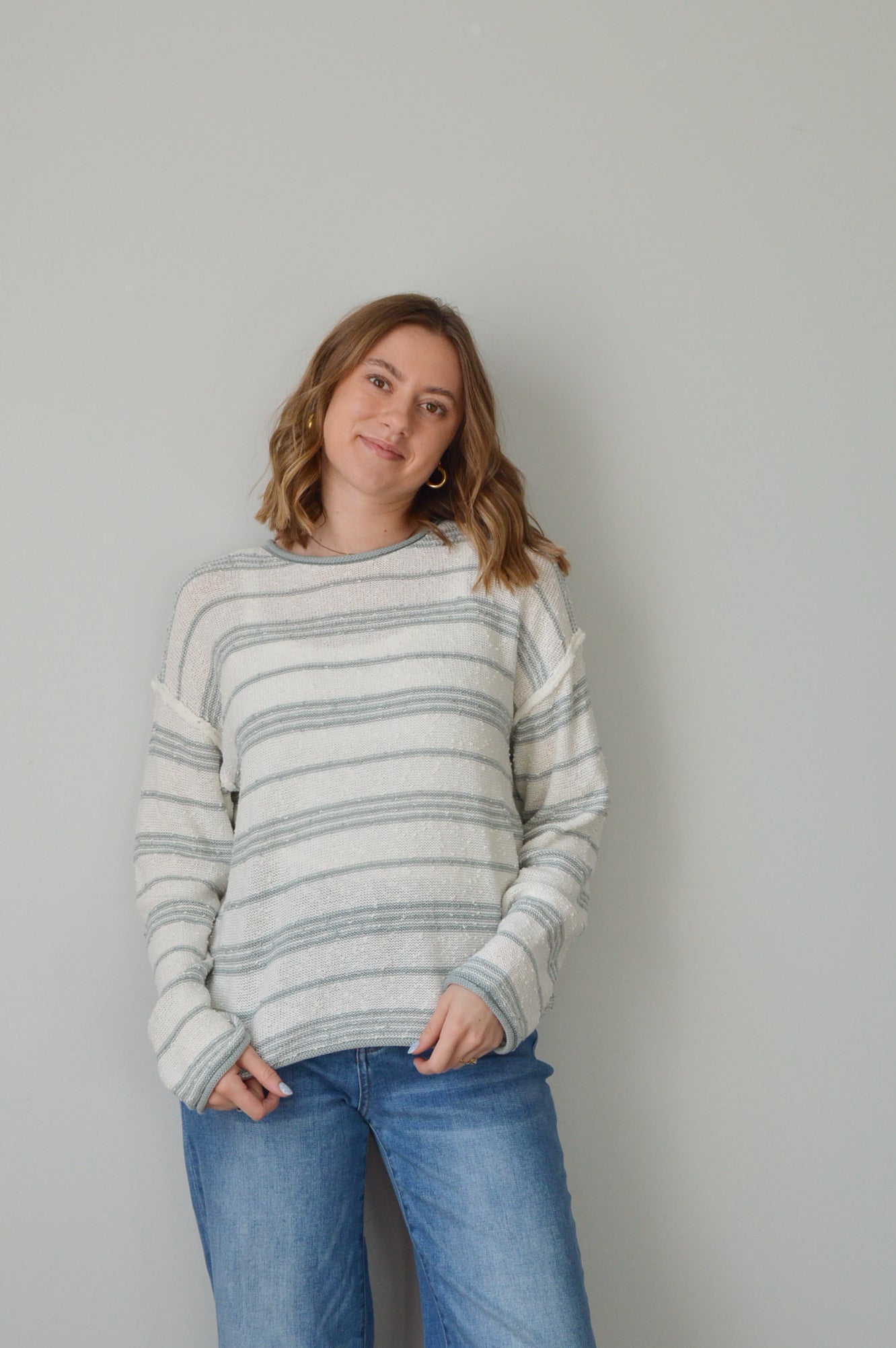 Person wearing a blue striped sweater and jeans on a plain background