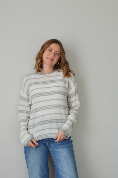 Person wearing a blue striped sweater and jeans on a plain background