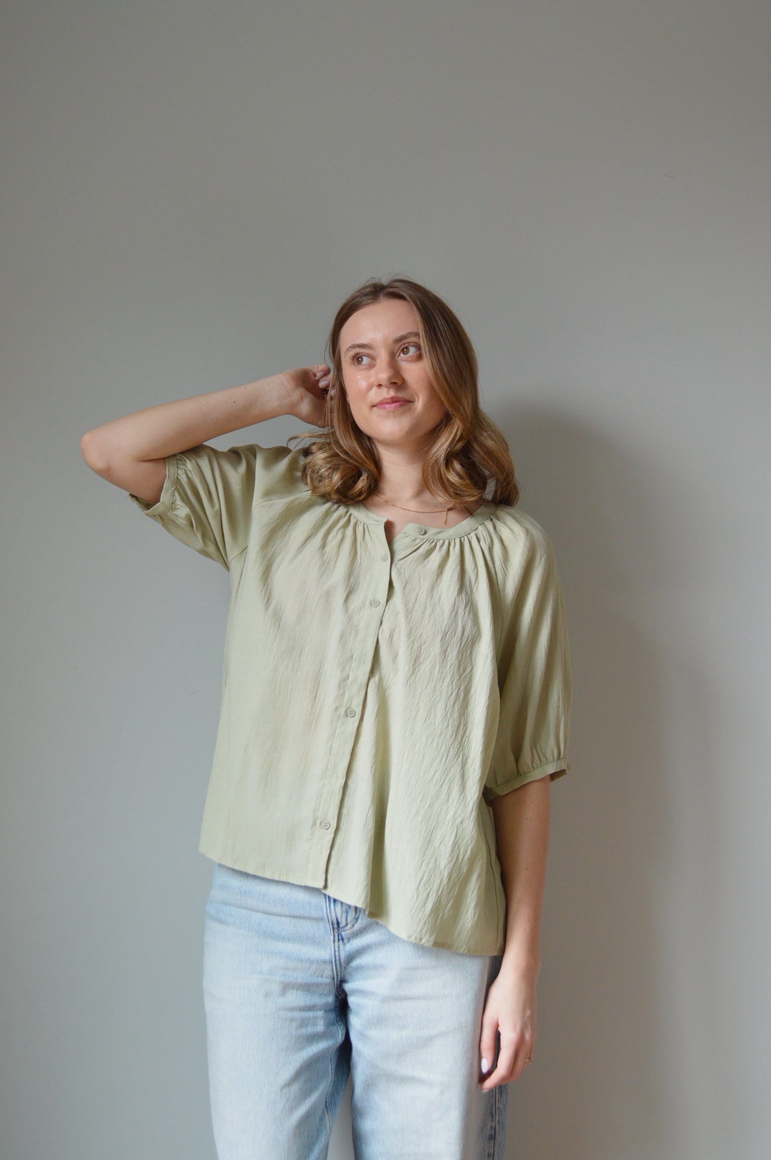 Woman wearing a light green blouse and blue jeans against a plain background