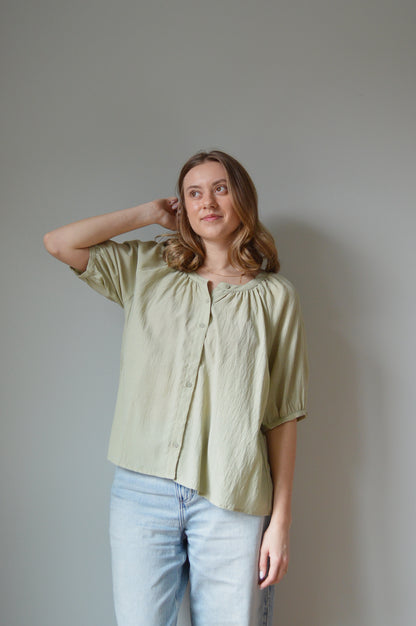 Woman wearing a light green blouse and blue jeans against a plain background