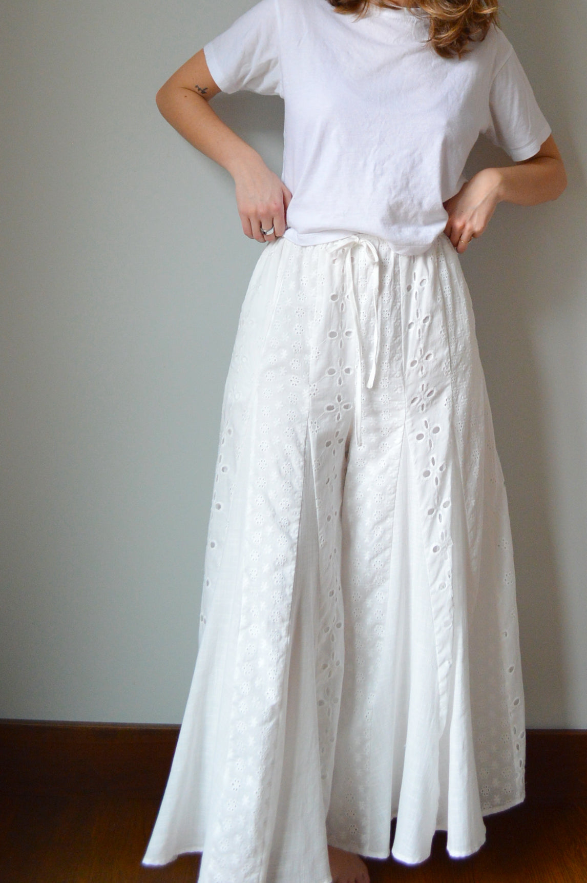 Woman wearing white eyelet wide leg pants standing against a plain background