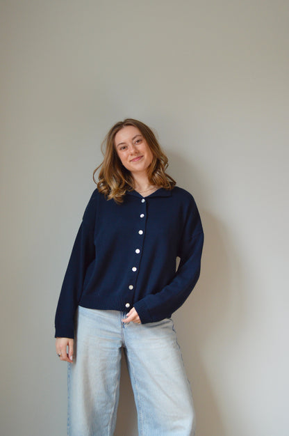 Person wearing a navy sweater with pearl buttons on a plain background