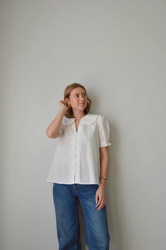 Woman wearing a white blouse and blue jeans against a plain background