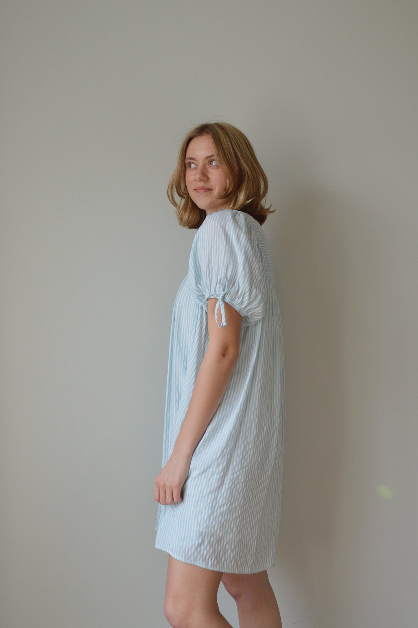 Woman wearing a light striped blue dress against a plain background
