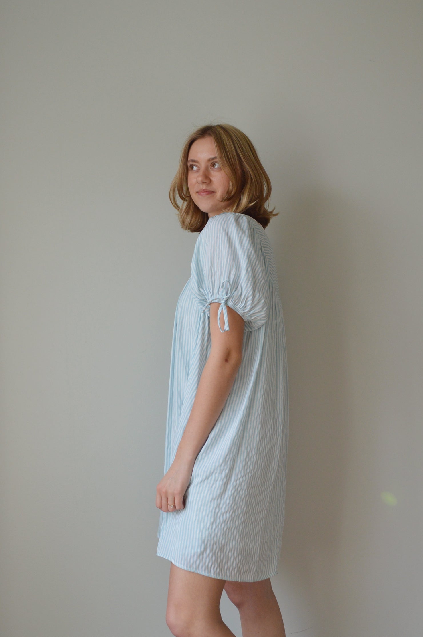 Woman wearing a light striped blue dress against a plain background