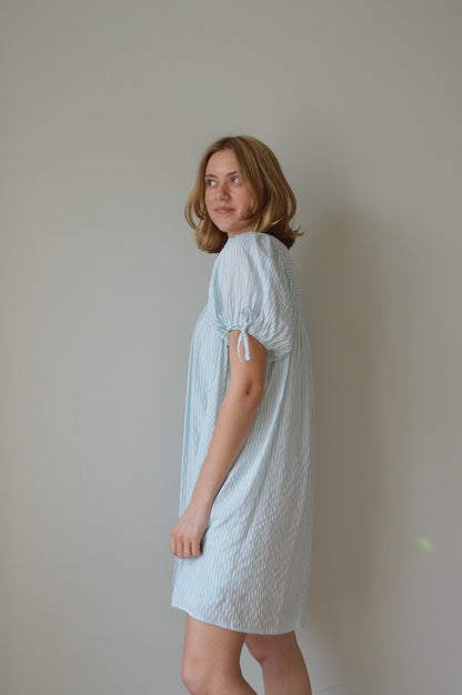 Woman wearing a light striped blue dress against a plain background
