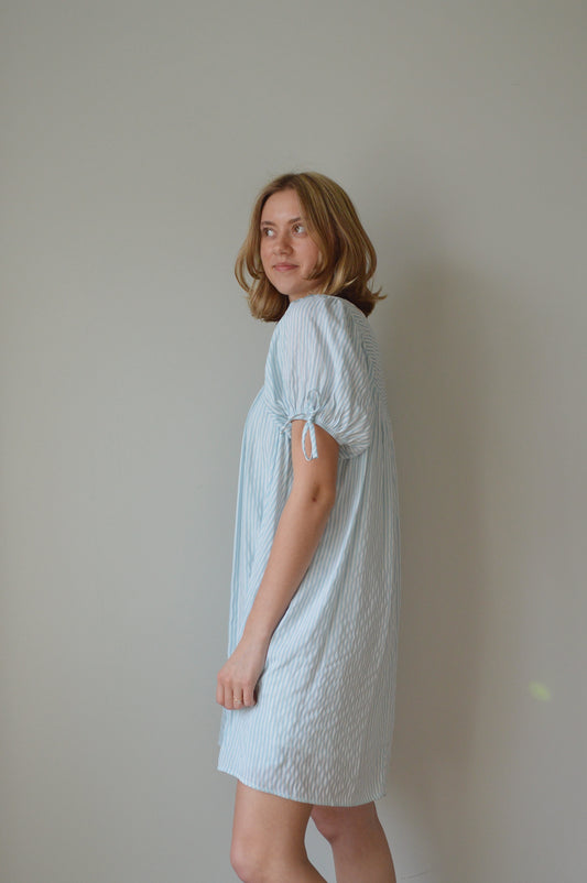 Woman wearing a light striped blue dress against a plain background