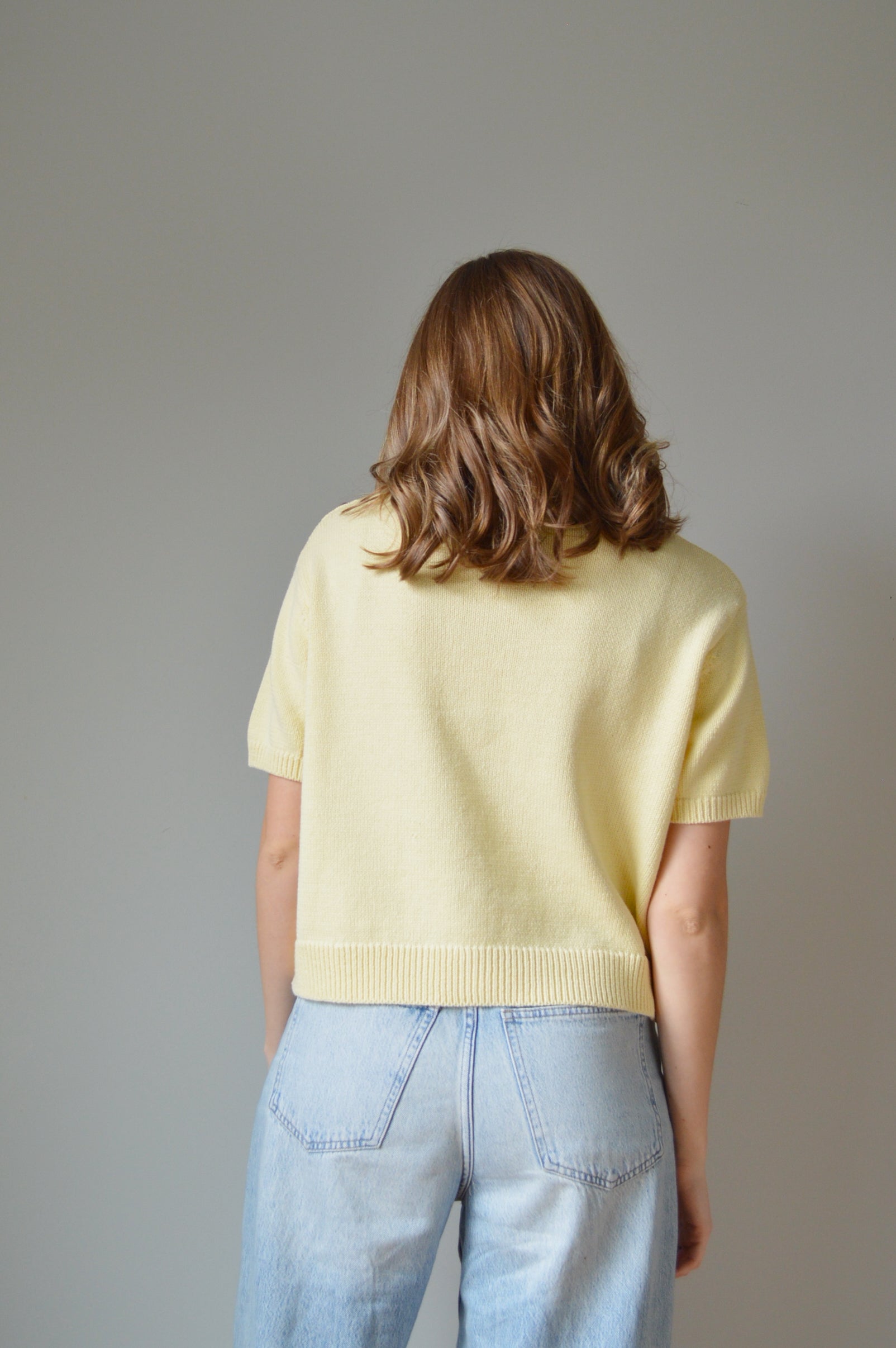 Person wearing a yellow sweater and blue jeans against a gray background