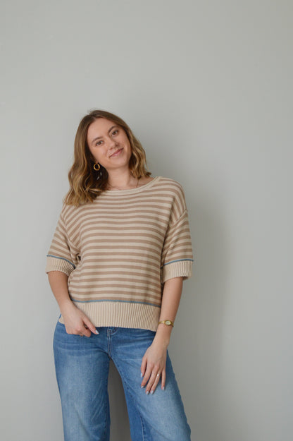 Woman wearing a tan striped sweater and blue jeans against a plain background