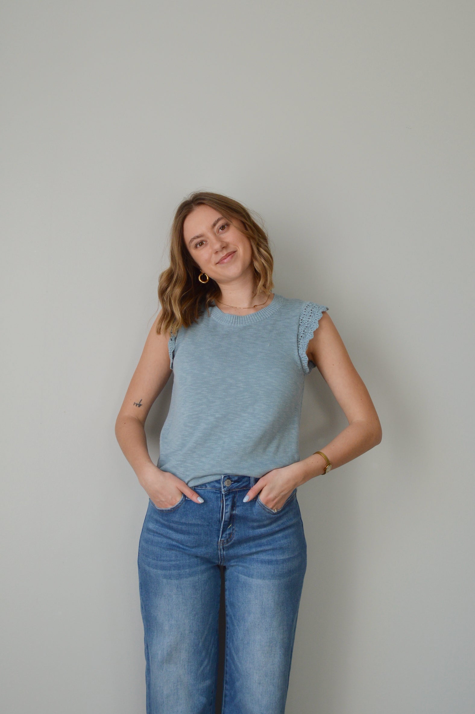Woman wearing a light blue top and jeans on a plain background