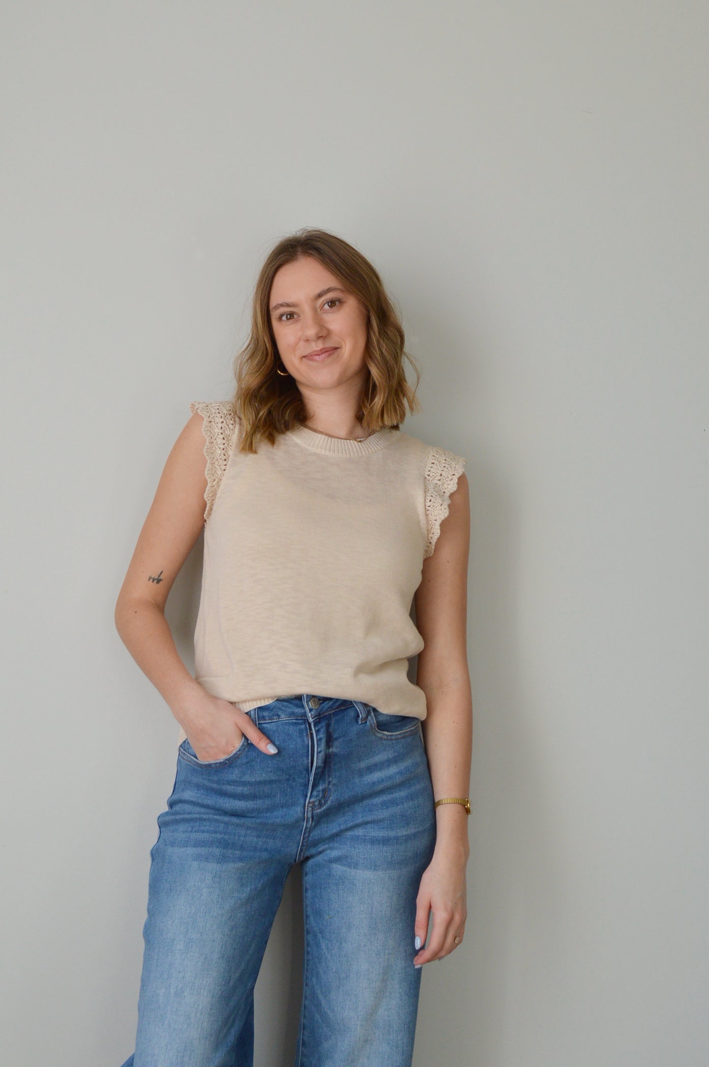Woman wearing a beige top and blue jeans against a plain background