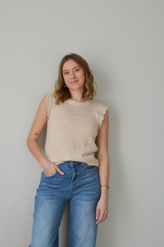 Woman wearing a beige top and blue jeans against a plain background
