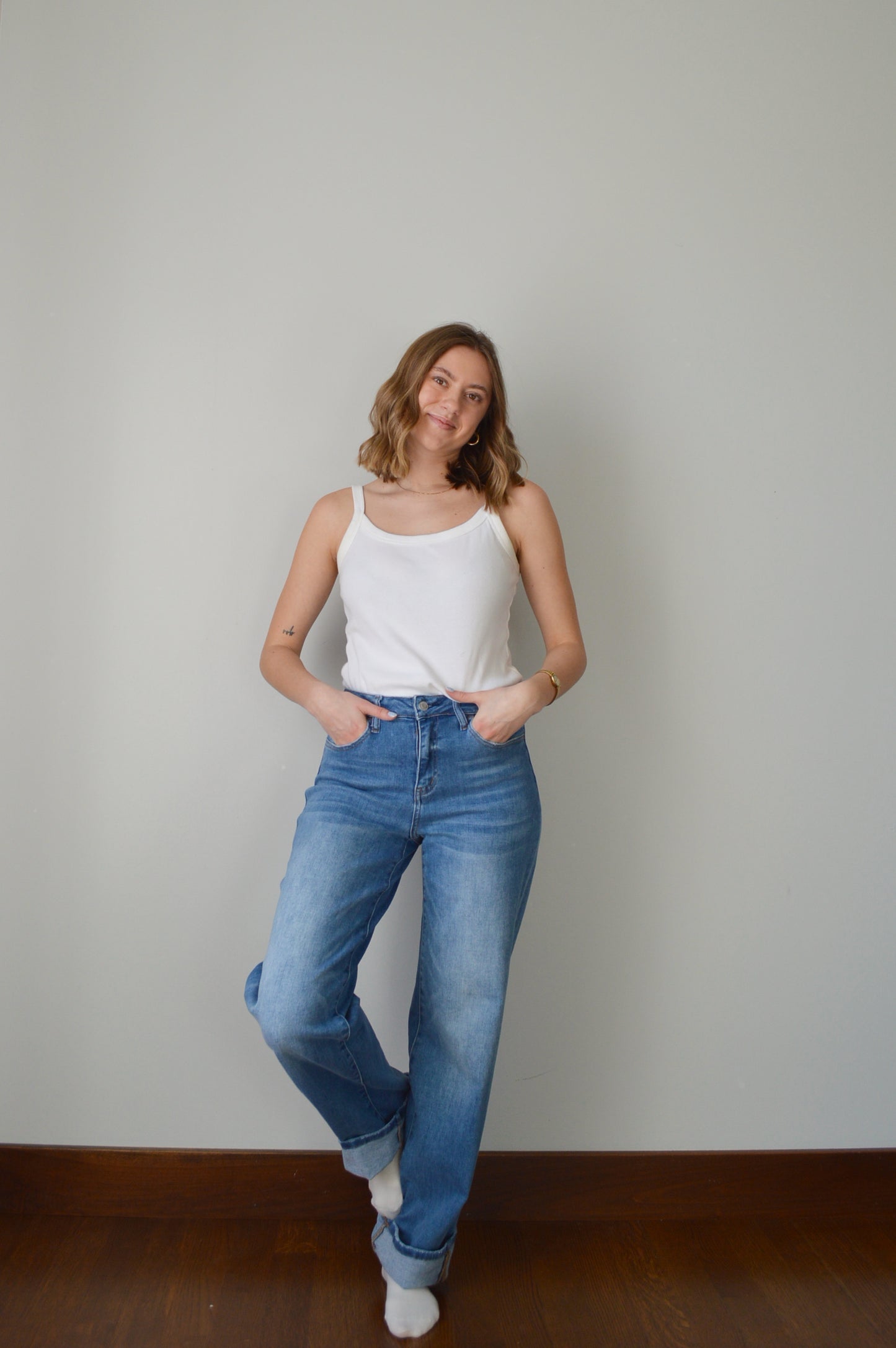 Person wearing blue cuffed jeans and a white top against a plain background