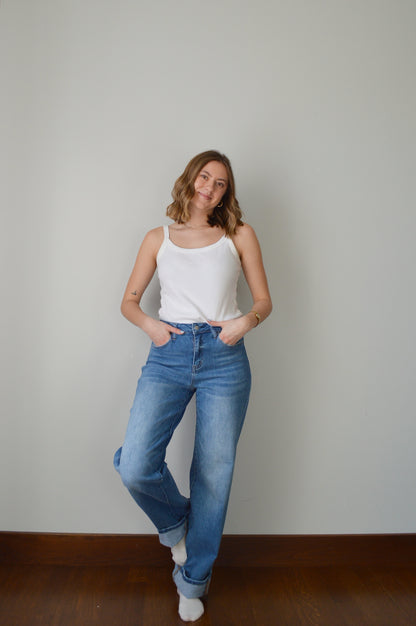 Person wearing blue cuffed jeans and a white top against a plain background