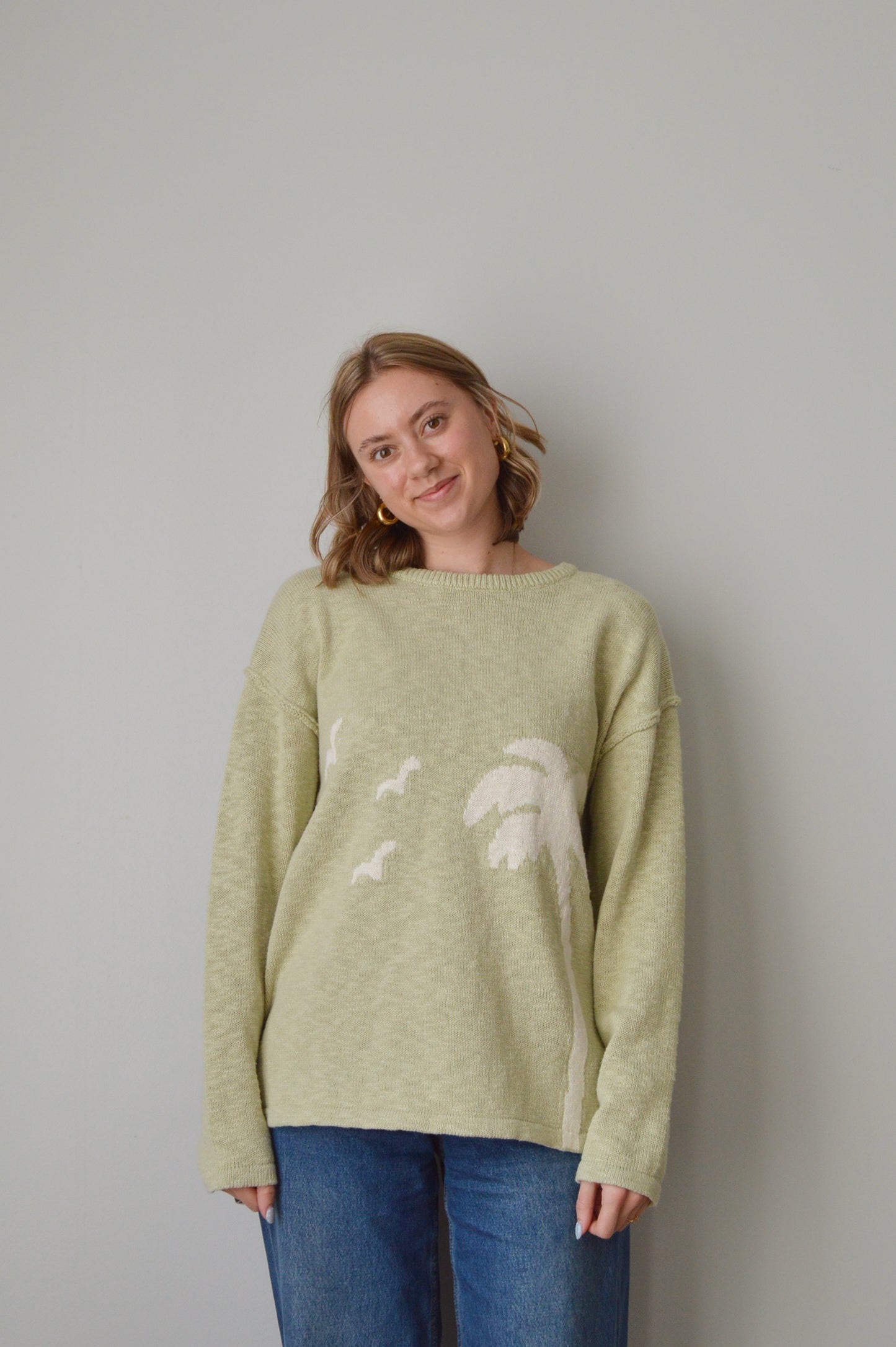 Person wearing a light green sweater with a palm tree pattern on a plain background