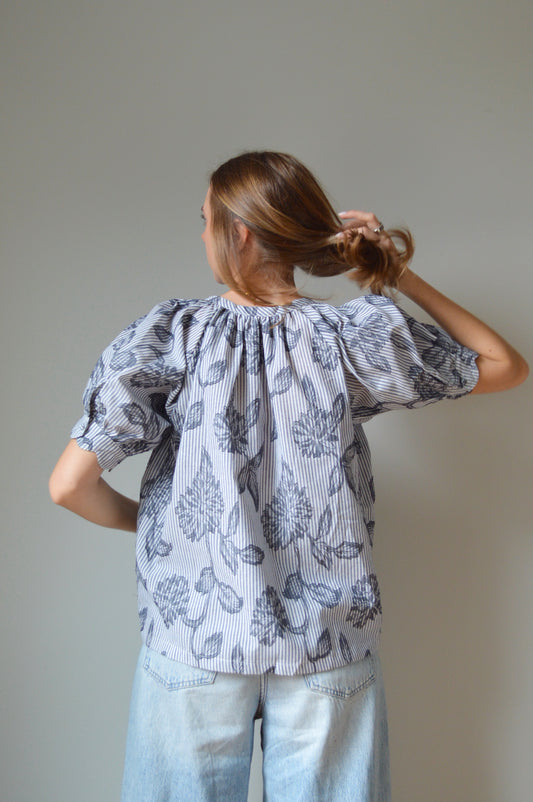 Woman wearing a blue striped blouse with navy floral design and jeans against a plain background