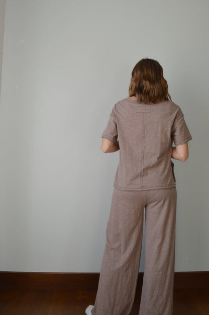 Person standing backwards wearing a brown outfit against a plain background