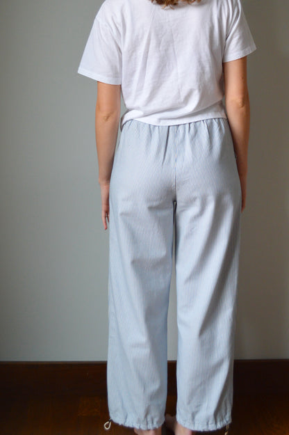 Woman wearing light blue and white striped pants against a gray wall