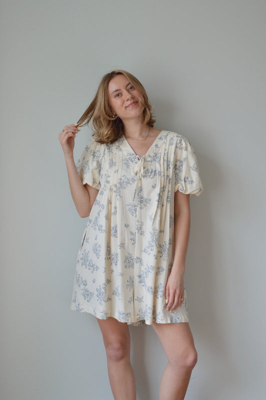 Woman wearing a cream romper with a blue floral pattern against a plain background 