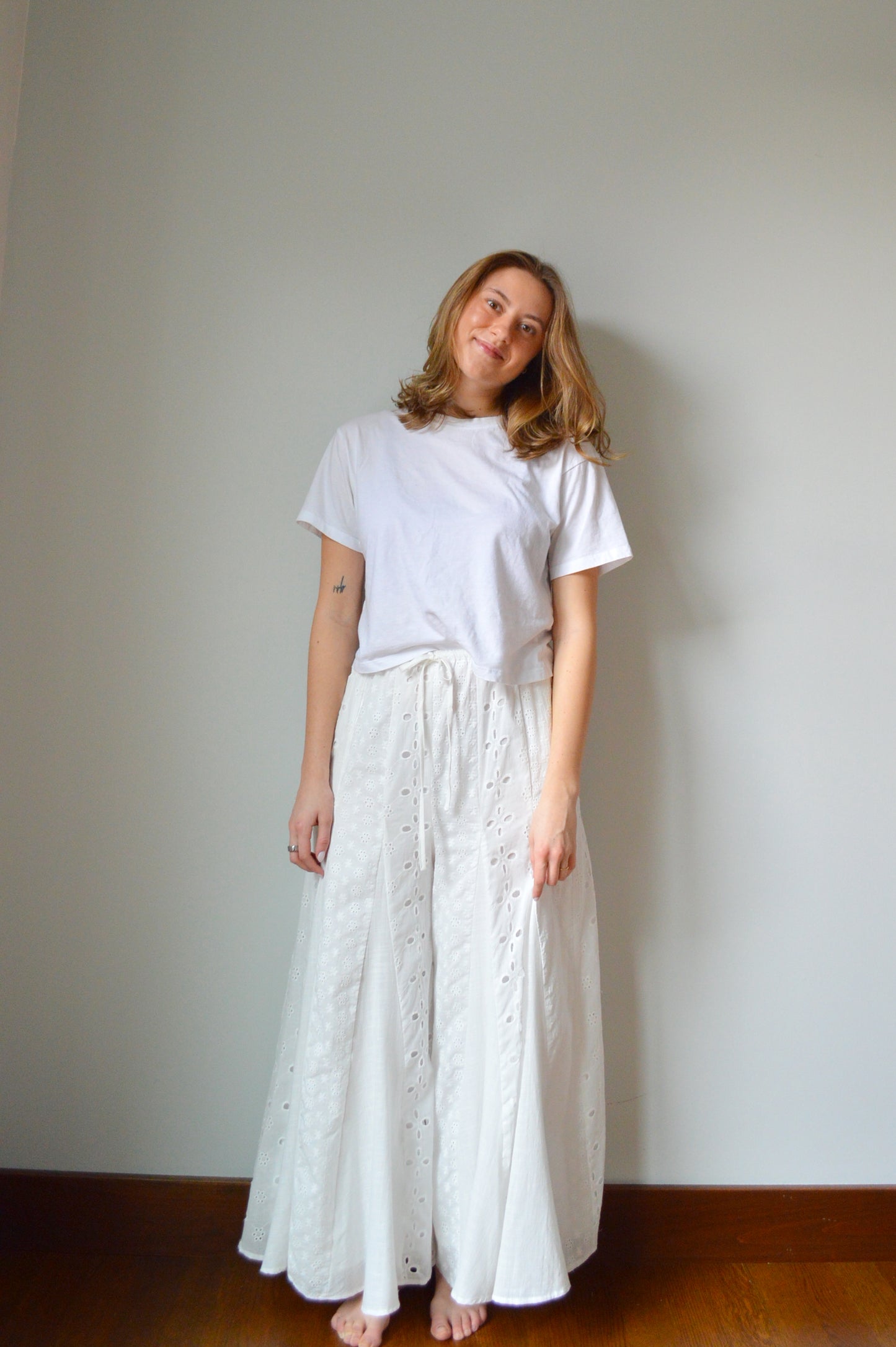 Woman wearing white eyelet wide leg pants standing against a plain background