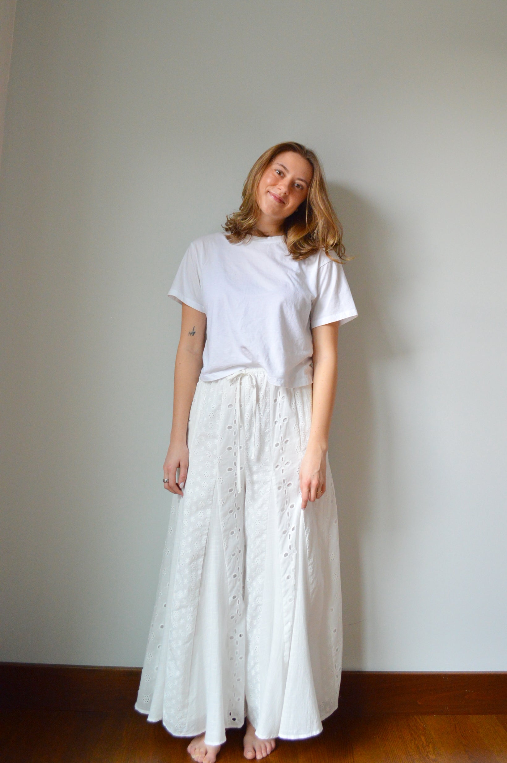 Woman wearing white eyelet wide leg pants standing against a plain background
