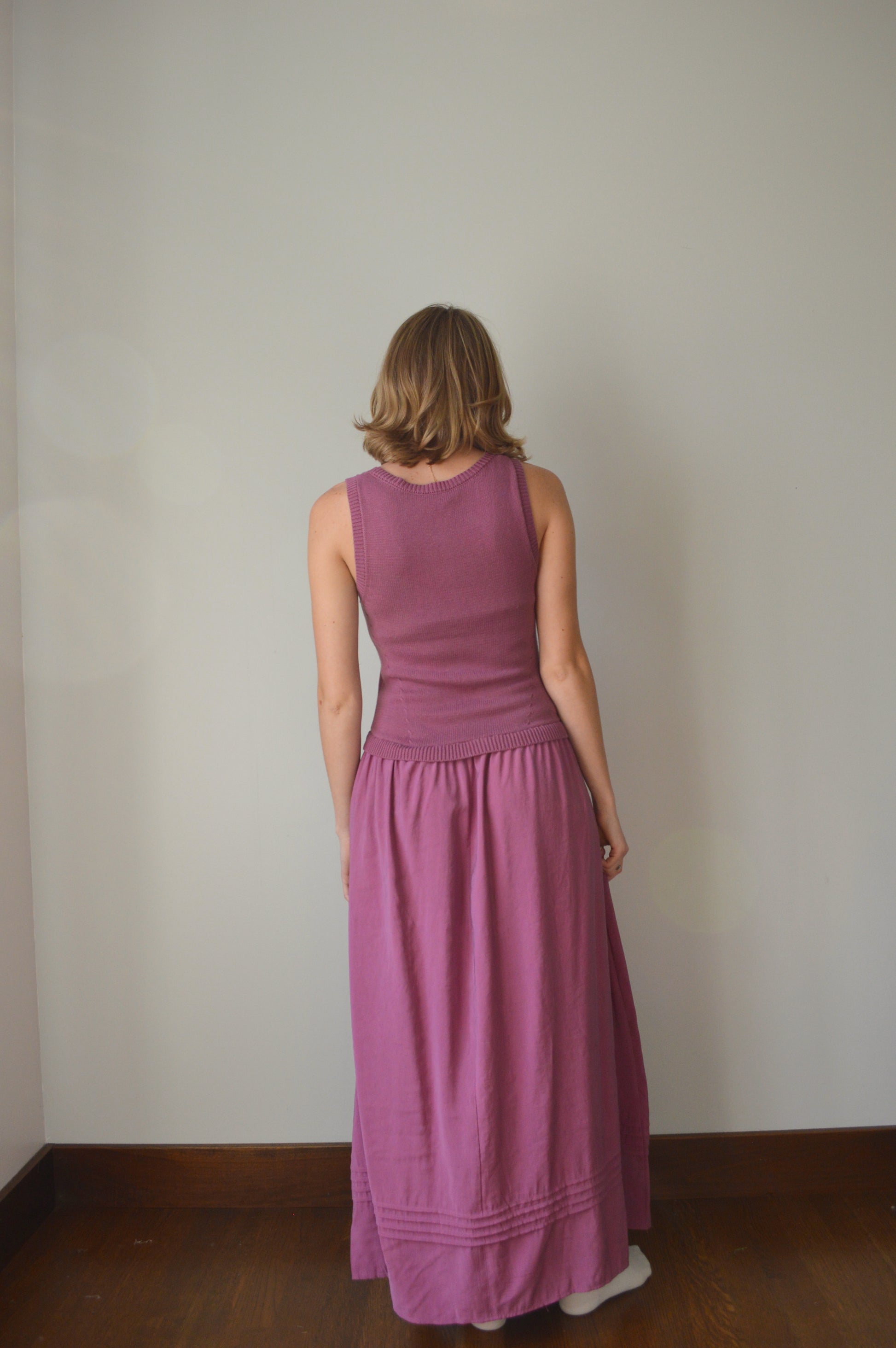 Person wearing a purple dress standing against a plain wall.